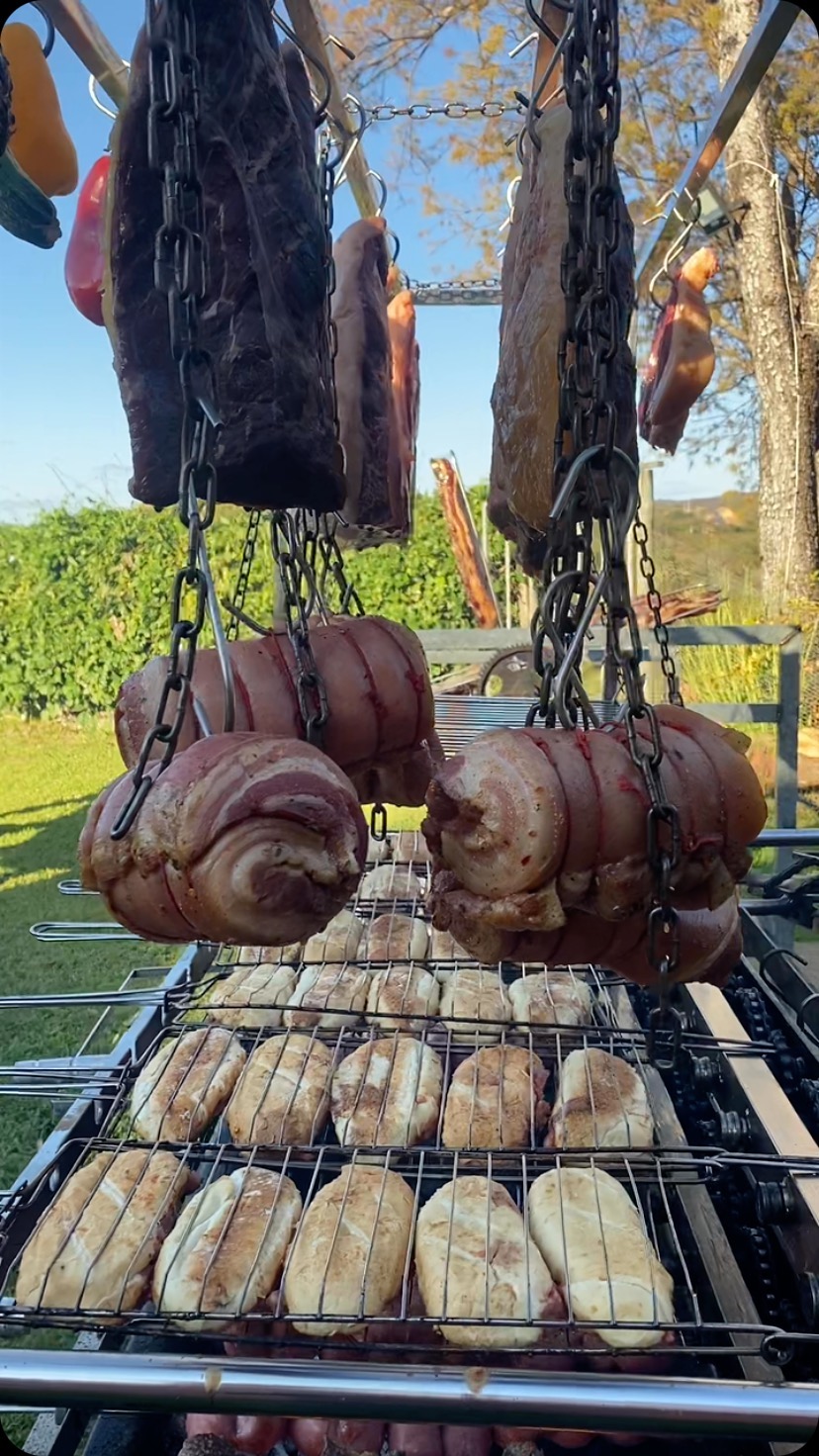 Peças de leitão penduradas em ganchos ao redor do fogo de chão.